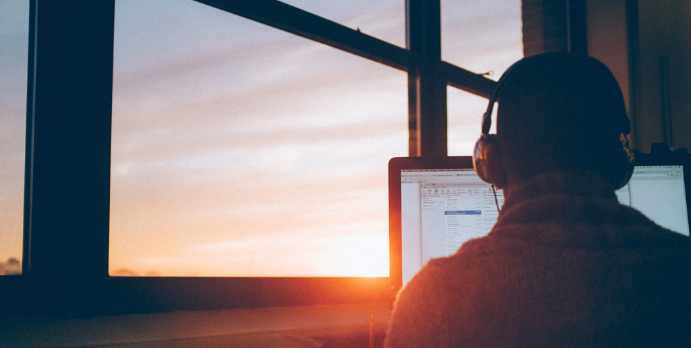 A man sitting at a computer as the sun sets in the background