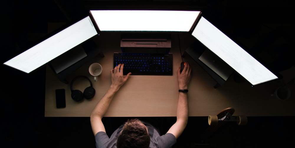 man sitting in front of 3 monitors